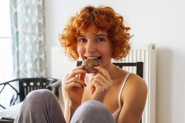 La donna è seduta sulla sedia a mangiare un biscotto.