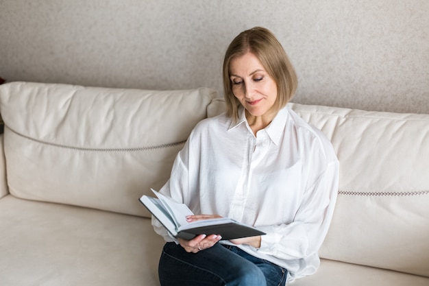 La donna è seduta tenendo un libro in mano e leggendo.