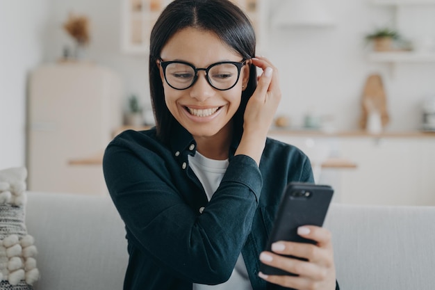 La donna eccitata che tiene in mano lo smartphone ha ricevuto un buon messaggio di notizie nei social network seduti sul divano di casa