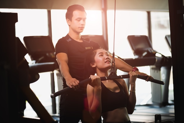 La donna esegue con la macchina di esercizio con un addestratore personale in palestra.