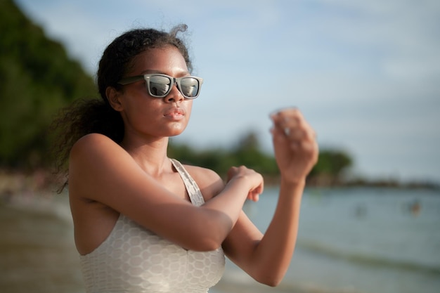 La donna esercita e allunga i muscoli prima dell'allenamento all'aperto Ritratto sexy signora africana asiatica che si prepara per il fitness in spiaggia