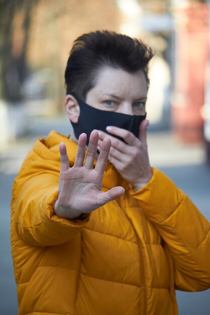 La donna europea di mezza età in maschera protettiva nera fa un gesto di avvertimento