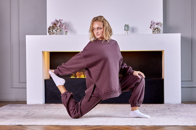 La donna europea fa esercizi di yoga vicino al camino a casa