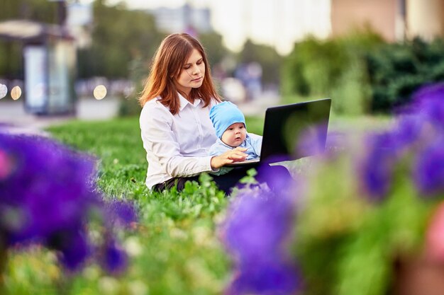 La donna fa il lavoro a distanza con il bambino sulle ginocchia nel giardino della città