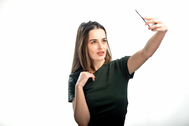 La donna fa un selfie in uno studio con una smartphome Bruna con una mano vicino al mento