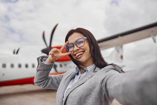 La donna felice caucasica sta sorridendo vicino all'aereo prima dell'imbarco?