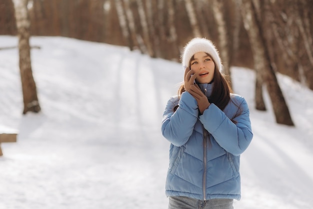 La donna felice chiama il cellulare mentre cammina nel parco invernale