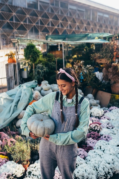 La donna felice dell'agricoltore in una tuta di jeans tiene la zucca matura