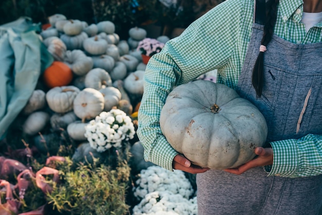 La donna felice dell'agricoltore in una tuta di jeans tiene la zucca matura