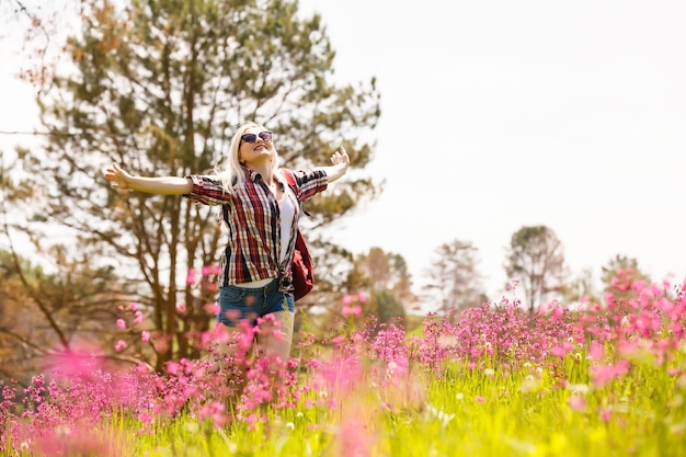 La donna felice dell'avventuriero si trova sul pendio verde della montagna tra i rododendri rosa in fiore e guarda in lontananza. Viaggio epico in montagna. Angolo ampio.