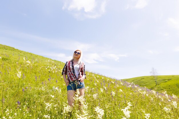 La donna felice dell'avventuriero si trova sul pendio verde della montagna tra i rododendri rosa in fiore e guarda in lontananza. Viaggio epico in montagna. Angolo ampio.