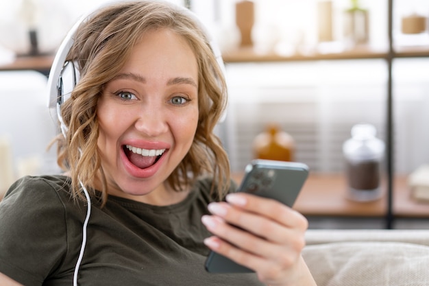 La donna felice di sorriso dei denti ascolta le cuffie di musica che tengono smartphone in mano