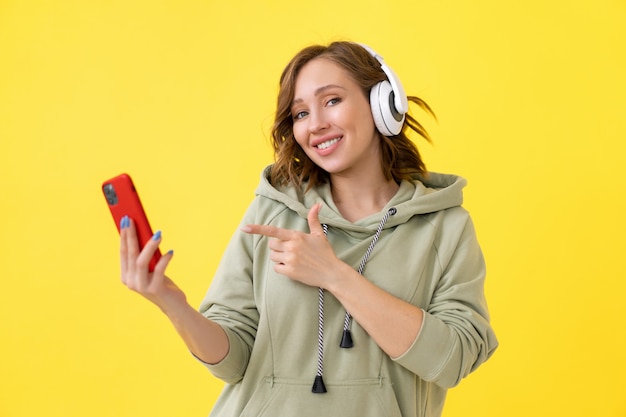 La donna felice di sorriso dei denti ascolta le cuffie di musica che tengono smartphone in mano