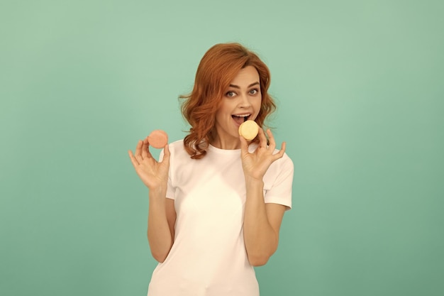 La donna felice mangia il biscotto francese dolce del macaron su fondo blu