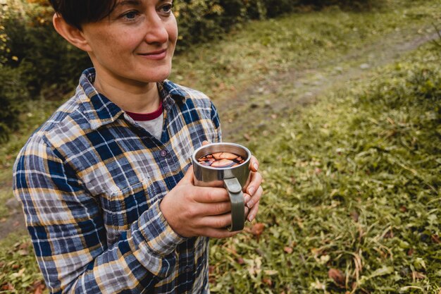 La donna felice passeggia nel parco autunnale con una tazza di vin brulé caldo