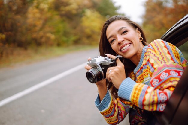 La donna felice scatta foto sulla fotocamera dal finestrino dell'auto Godersi il clima autunnale Concetto di stile di vita riposante