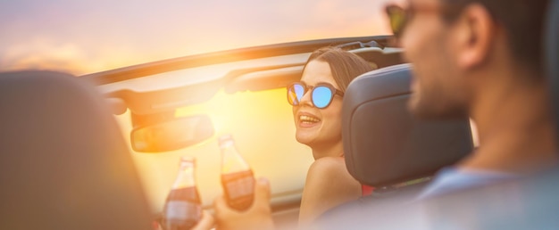 La donna felice si siede con gli amici in una cabrio sullo sfondo del sole splendente