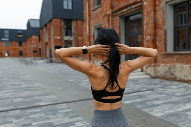 La donna fitness muscolare si riscalda per strada con le mani dietro la testa