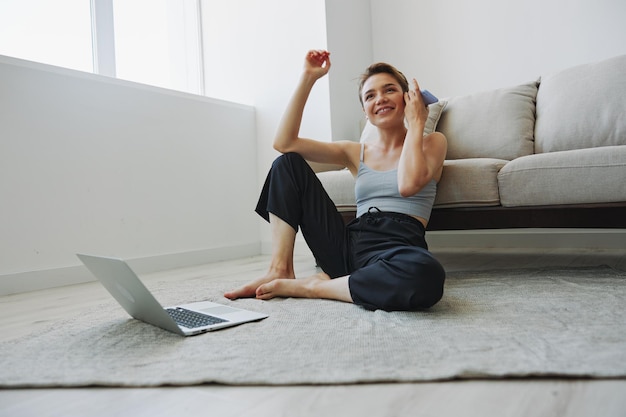 La donna freelance con laptop e telefono lavora da casa seduta sul pavimento nei suoi vestiti di casa con uno spazio di copia gratuito per il taglio di capelli corto