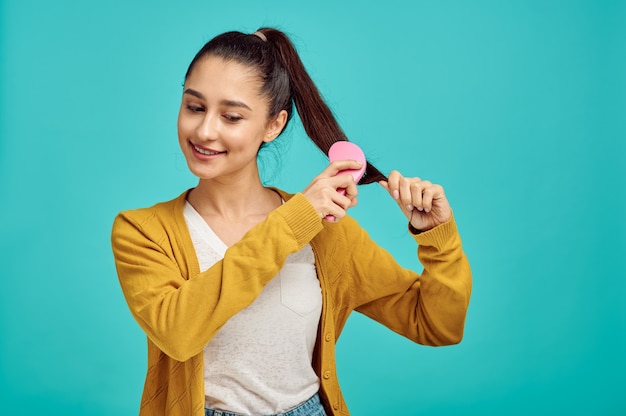 La donna graziosa si pettina i capelli, la parete blu, l'emozione positiva