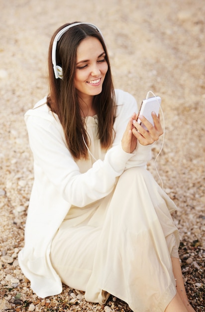 La donna graziosa sorridente si rilassa la musica d'ascolto con il telefono bianco