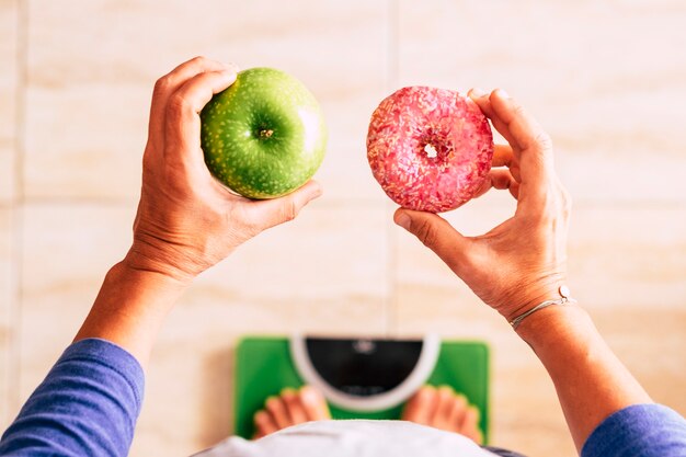 La donna guarda la ciambella e la mela per selezionare il suo stile di vita nutrizionale: è su una bilancia