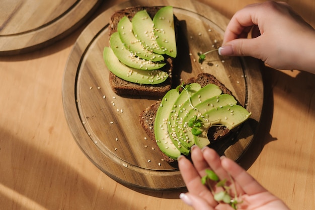 La donna ha messo le piantine di senape sul panino di avocado con pane di segale scuro fatto con avocado affettato fresco