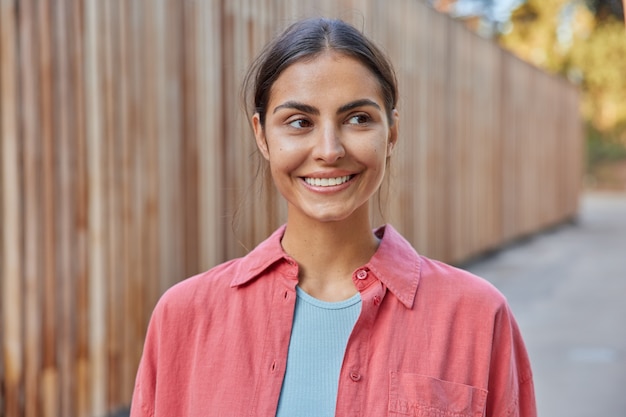 la donna ha un sorriso allegro sul viso sorride e guarda in lontananza vestita casualmente gode di un bel tempo soleggiato durante la primavera indossa abiti casual. Emozioni delle persone e concetto di stile di vita.