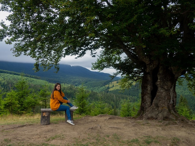 La donna in abiti casual si siede sotto un grande albero con sfondo forestale