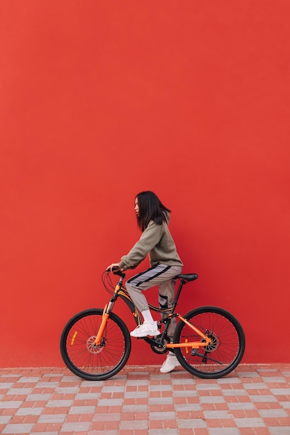 La donna in abiti casual va in bicicletta su uno sfondo rosso