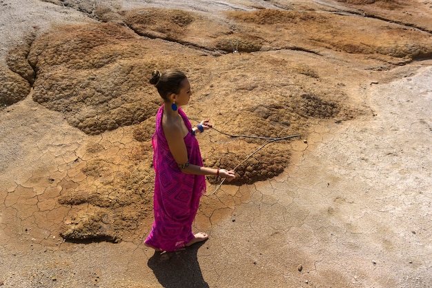 La donna in abiti etnici orientali cerca l'acqua in una zona desertica con il metodo della rabdomanzia