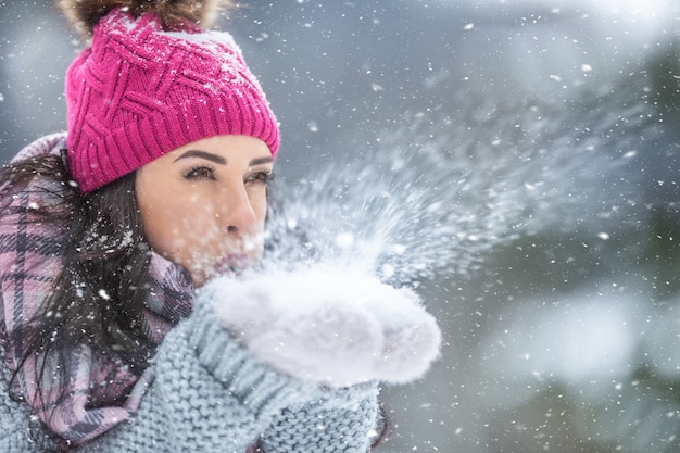 La donna in abiti invernali soffia via la neve dalle mani all'aperto.