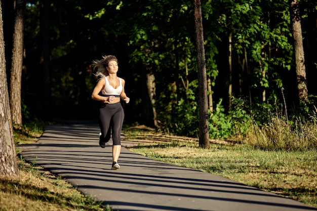 La donna in abiti sportivi corre su strada nella foresta in estate