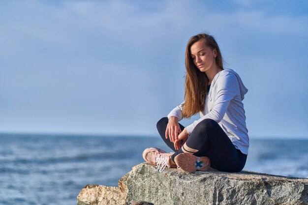 La donna in abiti sportivi si siede su una scogliera