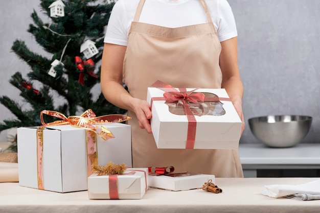 La donna in abito da cucina tiene scatole regalo con dolci natalizi. Dolci regali per le feste.