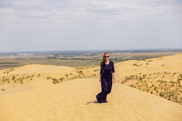 La donna in abito lungo nero cammina attraverso le dune del deserto in estate con la schiena