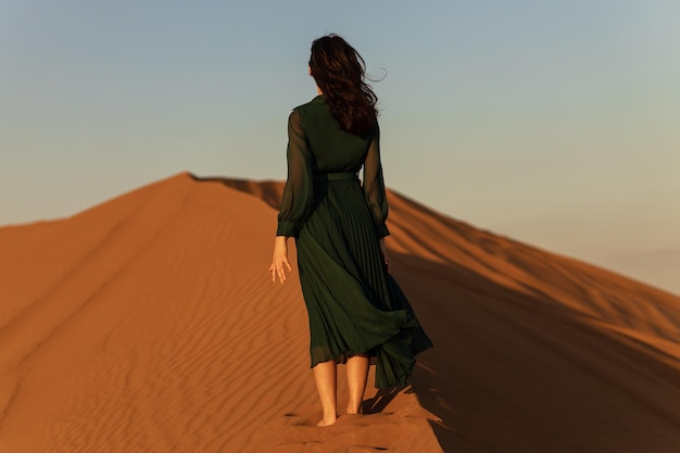 La donna in abito lungo verde si trova nel tramonto giallo arancione delle dune di sabbia del deserto