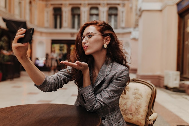 La donna in abito scozzese soffia un bacio e si fa un selfie nel caffè della città