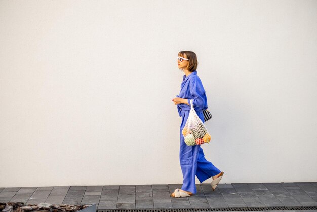 La donna in blu cammina con una borsa a rete piena di cibo fresco