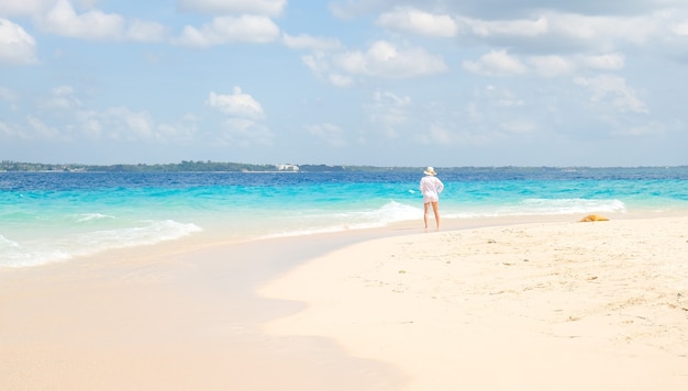 La donna in camicia bianca sta sulla riva e guarda l'oceano