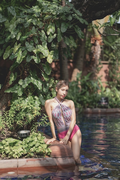 La donna in costume da bagno intero rosa si rilassa nella piscina tropicale, vacanze estive
