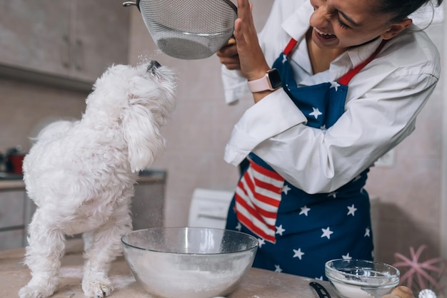 La donna in cucina setaccia la farina insieme a un cane