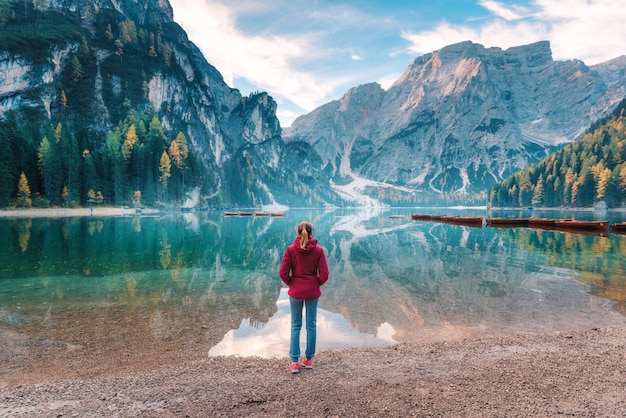 La donna in giacca rossa sta stando sulla costa del lago Braies all'alba in autunno. Dolomiti, Italia.