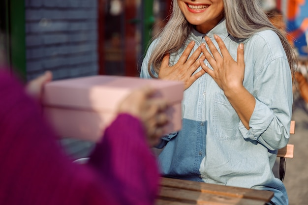 La donna in giacca viola fa un regalo a un felice amico dai capelli grigi seduto sulla terrazza del caffè all'aperto