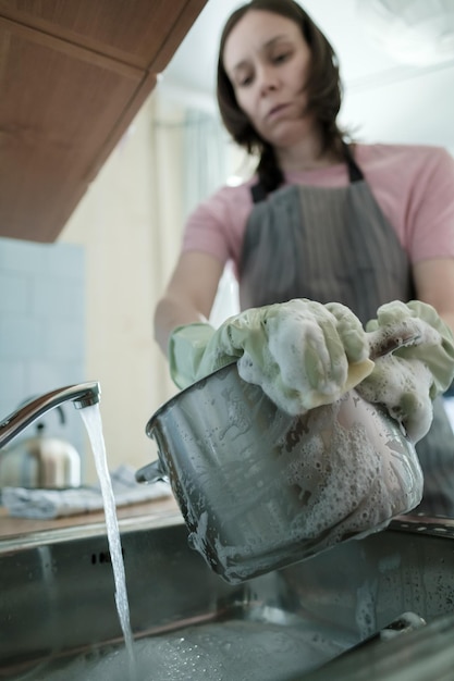 La donna in guanti di gomma verdi lava la padella nel lavandino in cucina