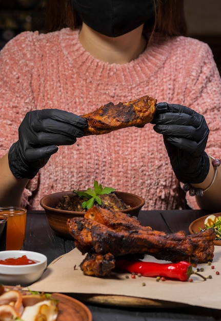 La donna in guanti neri inizia a mangiare costolette con pepe e una bottiglia di vino