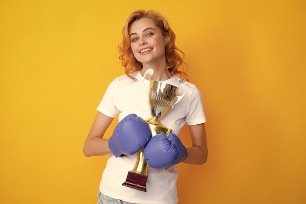 La donna in guantoni da boxe tiene il trofeo della coppa del vincitore del campione Pugile femminile del vincitore isolato su giallo