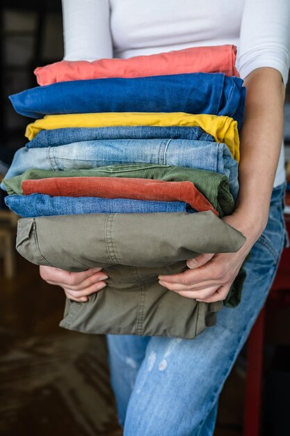 La donna in maglietta bianca tiene in mano ben piegata in una pila di pantaloni e jeans dai colori vivaci