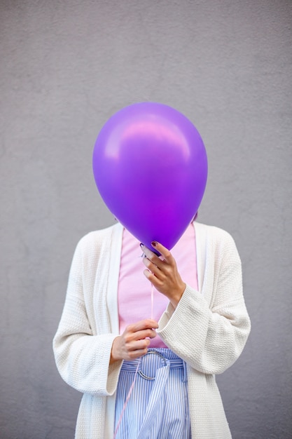 La donna in maglione bianco copre la testa con un palloncino viola