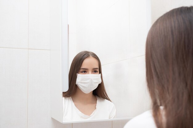 La donna in maschera medica si guarda allo specchio a casa in bagno